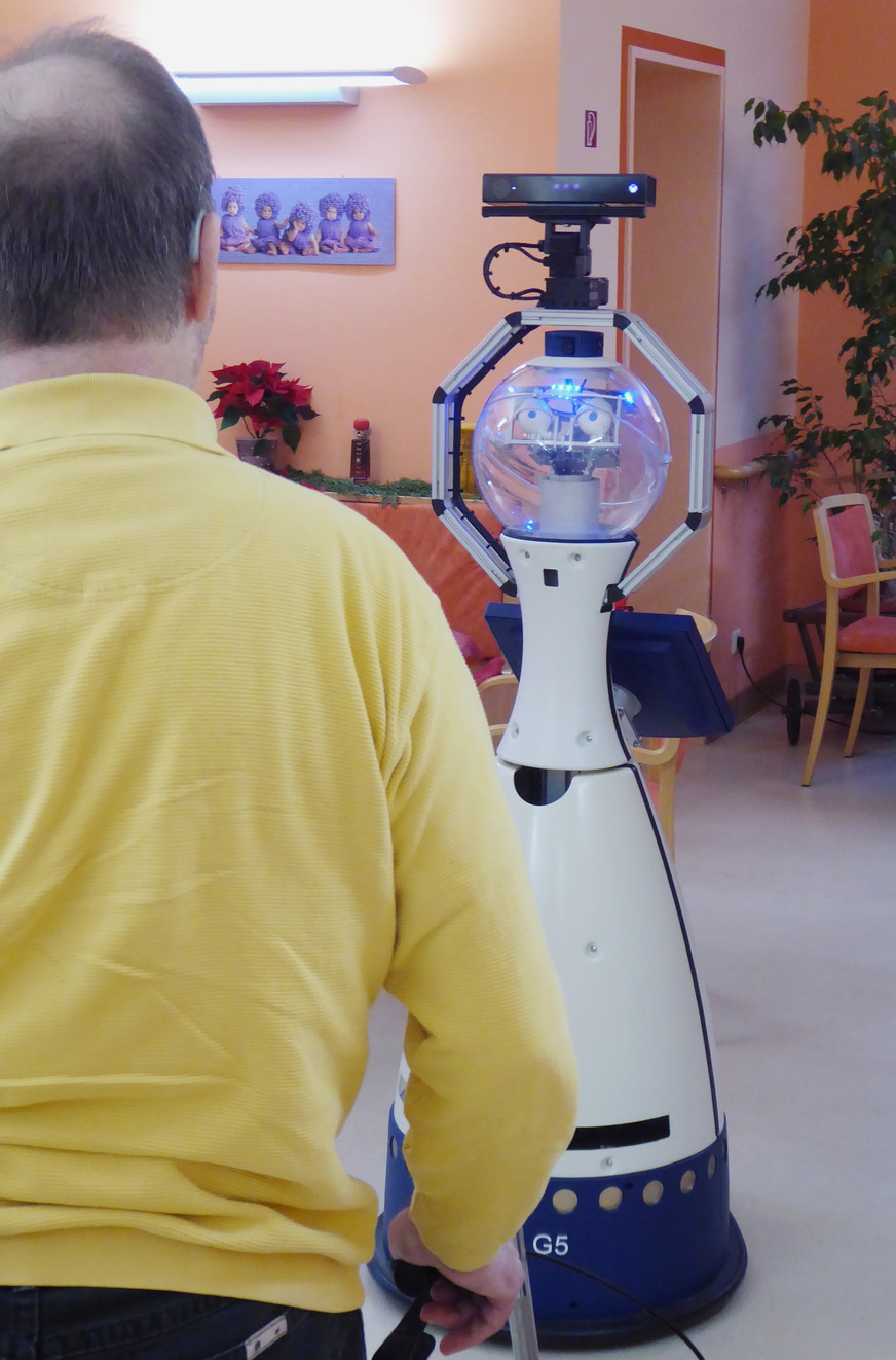 Abb. 2: Robotische Assistenzsysteme im Praxiseinsatz. Zu sehen ist Roboter Anna der HTW Dresden bei der morgendlichen Begrüßung eines Bewohners einer stationären Altenpflegeeinrichtung zu Beginn der Demenztherapie