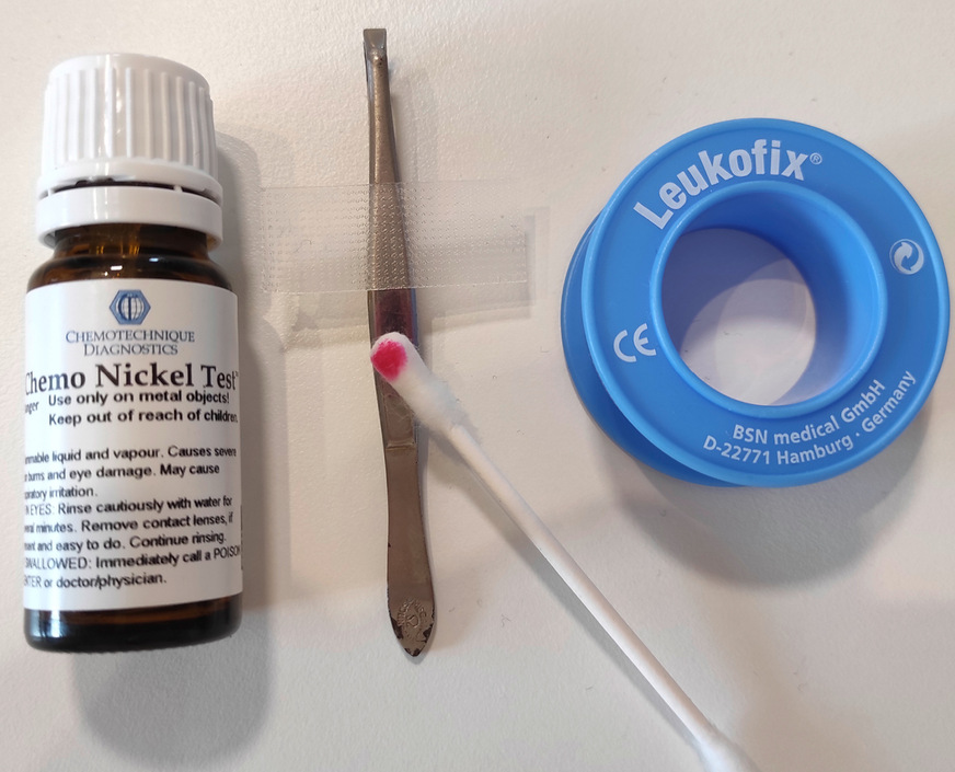 Abb. 1: Vorbereitete Teststellen, an denen ein längerer und unmittelbarer Hautkontakt gegeben ist (mithilfe von Leukofix®, BSN medical GmbH, Hamburg, Deutschland), an einer Pinzette zur Durchführung des Nickel- und Kobalt-Spot-Tests. Die Testung mit der ersten Testlösung kann oberhalb des Streifens Leukofix® erfolgen, die Testung mit der zweiten Testlösung entsprechend unterhalb des Streifens. Deutlich sichtbar ist der rötlich-pinke Farbumschlag des Nickel-Spot-Tests (hier: Chemo Nickel Test™, Chemotechnique Diagnostics®, Vellinge, Schweden), der in diesem Fall bereits nach wenigen Sekunden eintrat und ein positives Nickel-Testergebnis anzeigt