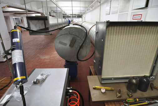 
 Abb. 4: 
 Nano Test Facility des IGF der BG RCI. Im Bild der Windkanal mit Aerosolgenerator im Vorder-grund und Probenahmeraum am hinteren Ende. Hier können gleichzeitig verschiedenste Messgeräte definierten nanomaterialhaltigen Atmosphären ausgesetzt werden
