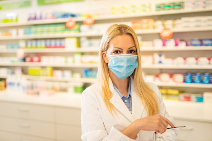 Female mid adult healthcare worker wearing a protection mask in pharmacy house.