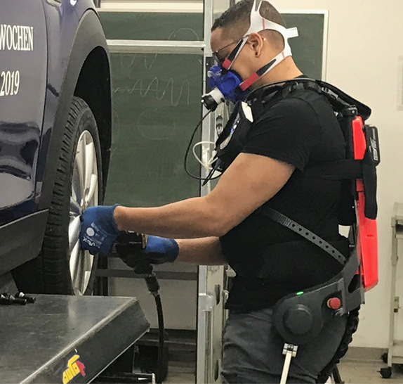 Abb. 1:    Mechaniker bei der Radmontage, ausgestattet mit dem mobilen Ergospirometrie-System Cortex MetaMax 3B-R2 und dem aktiven Exoskelett „Cray X“