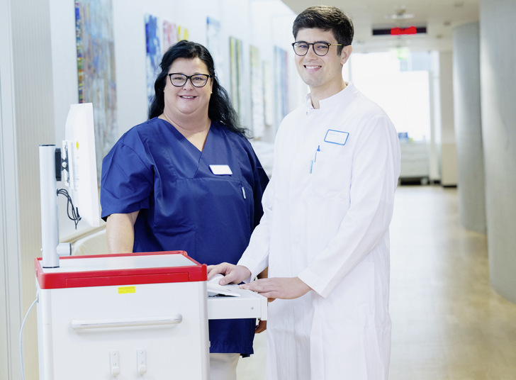 Arzt und Pflegekraft am mobilen Visitenwagen: Die Kommunikation miteinander, die Zusammenarbeit im Team und die Förderung gesundheitsförderlicher Führung sind wichtige Pfeiler sozialer Beziehungen