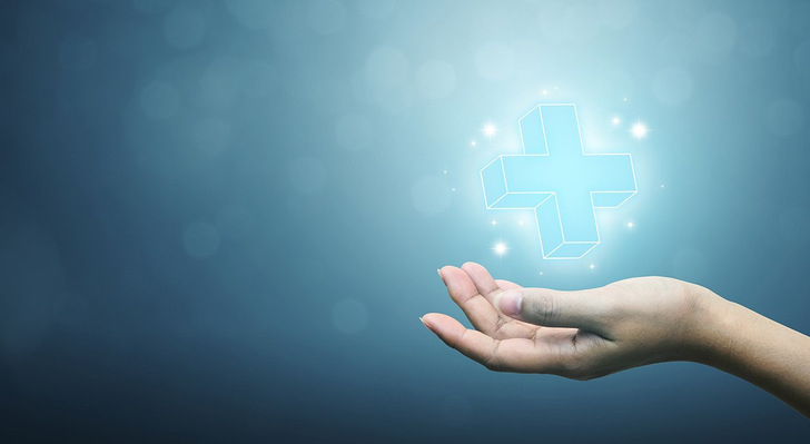 Eine Hand streckt sich nach einem leuchtenden medizinischen Kreuzsymbol auf blauem Hintergrund aus. - © Monster Ztudio - stock.adobe.com