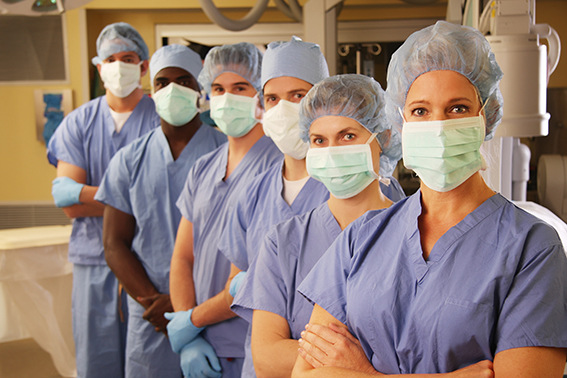 "Medical team stands in with hospital operating room in background, with scrubs, and operating face masks. I left the space on the left for text or logo info."