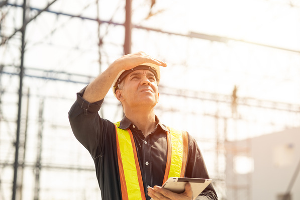 Foreman builder engineer worker looking at large building construction site sunny day hard work.
