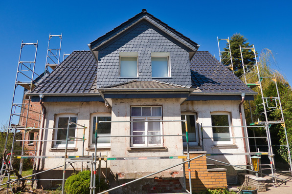 Alt-Text: „Arbeiter in Schutzkleidung führen Renovierungsarbeiten an einem Gebäude durch, das mit Gerüsten gesichert ist. Fokus auf Arbeitsschutzmaßnahmen und ergonomische Praktiken im Bauwesen. - © Shutterstock / Frank Oppermann