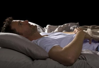 Alt-Text: „Ein gestresster Arbeitnehmer liegt mit offenen Augen im Bett, symbolisiert die Auswirkungen ergonomischer Arbeitsplatzgestaltung auf den Schlaf und die Gesundheit, relevant für betriebliche Gesundheitsmanager und Arbeitsmediziner.“. - © Innovated Captures – stock.adobe.com