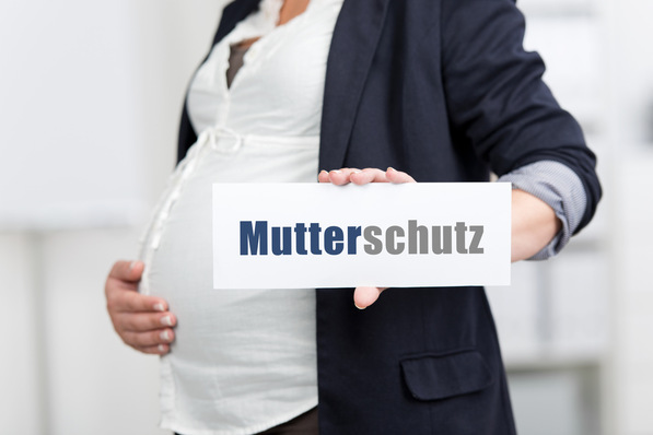Alt-Text: „Schwangere Frau im Blazer hält ein Schild mit der Aufschrift ‚Mutterschutz‘, symbolisiert die Bedeutung von Arbeitsschutz und präventiven Maßnahmen für werdende Mütter im betrieblichen Gesundheitsmanagement.“. - © contrastwerkstatt - stock.adobe.com