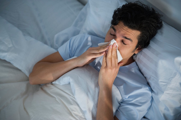 Alt-Text: „Erkrankte Person im Bett, symbolisiert die Bedeutung präventiver Maßnahmen und arbeitsmedizinischer Vorsorge zur Verhinderung krankheitsbedingter Ausfälle im Arbeitsumfeld.“. - © Copyright: DAK-Gesundheit