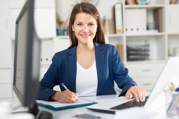 Arbeitsmedizinerin in einem blauen Blazer analysiert am Schreibtisch mit Laptop und Unterlagen aktuelle Leitlinien zu präventiven Maßnahmen im Arbeitsschutz als Teil des betrieblichen Gesundheitsmanagements. - © JackF - stock.adobe.com