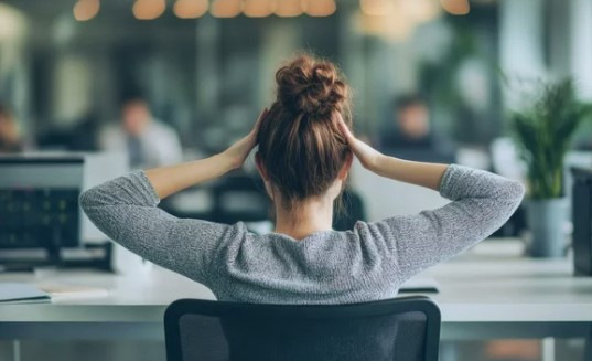 „Arbeitsmedizinerin mit Dutt sitzt nachdenklich im Büro und überlegt präventive Maßnahmen zur Verbesserung des betrieblichen Gesundheitsmanagements. - © Prompt2image – stock.adobe.com