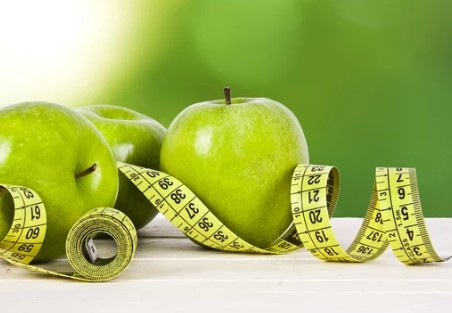 „Grüne Äpfel und ein gelbes Maßband auf Holztisch symbolisieren gesunde Lebensweise und präventive Gesundheitsmaßnahmen im betrieblichen Gesundheitsmanagement. - © carballo – stock.adobe.com