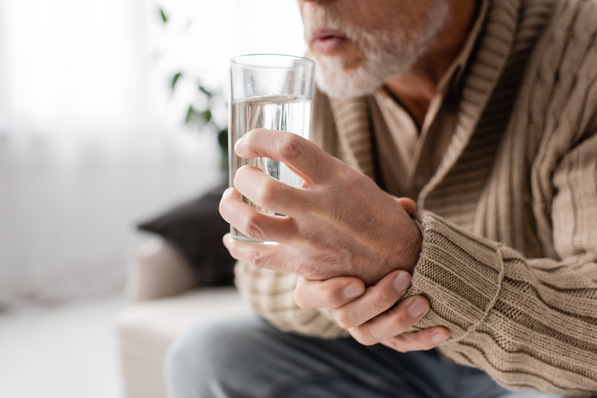„Ältere Person in beiger Strickjacke hält ein Glas Wasser in der Hand, symbolisiert die Bedeutung von ergonomischen Anpassungen und präventiver Gesundheitsvorsorge für ältere Beschäftigte am Arbeitsplatz.“. - © LIGHTFIELD STUDIOS - stock.adobe